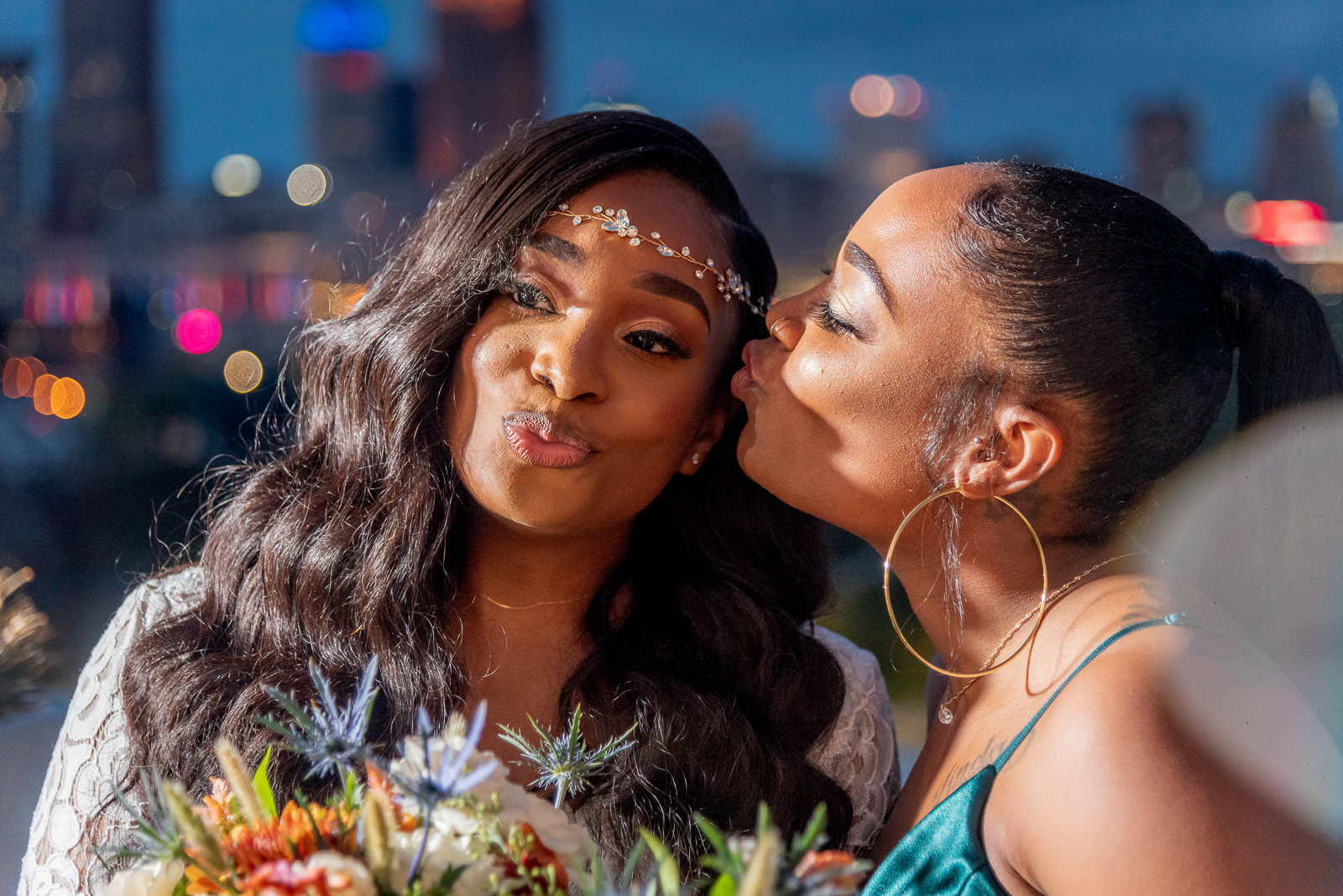 Bride with bridesmaid, bridal party portrait, kiss, sweet, candid, African American bride, African American wedding, night photography, night wedding photo, downtown Cleveland skyline, urban wedding ceremony at Penthouse Events, Ohio City, Cleveland Flats