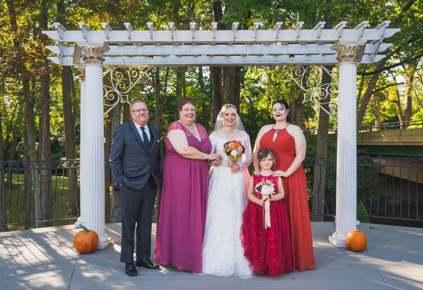 Bride with maid of honor, flower girl, mom and dad, parents of the bride, family portrait, wooden arch with columns, green, nature, trees, fall wedding, cute outdoor wedding ceremony at Grand Pacific Wedding Gardens