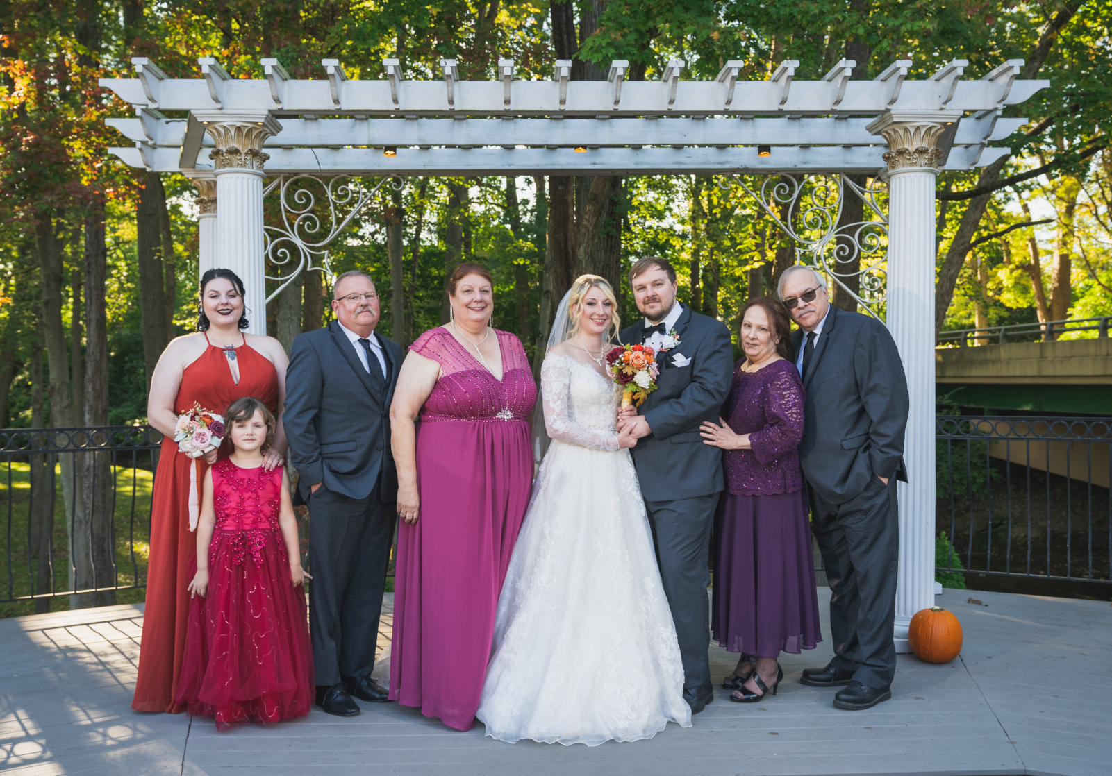 Bride and groom, maid of honor, flower girl, with family, family portrait, wooden arch with columns, nature, green, trees, fall wedding, cute outdoor wedding ceremony at Grand Pacific Wedding Gardens