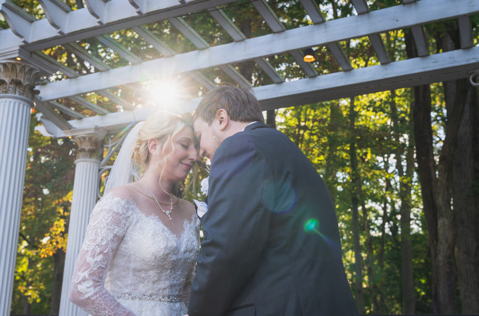 Bride and groom wedding portrait, couple portrait, sweet, sunlight, lens flare, wooden arch with columns, green, nature, trees, fall wedding, cute outdoor wedding ceremony at Grand Pacific Wedding Gardens