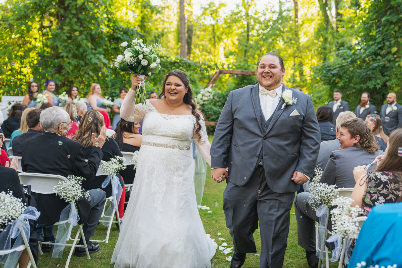 Bride and groom smiling, wedding recessional, hexagon arch, green, nature, trees, outdoor September wedding ceremony at Westfall Event Center