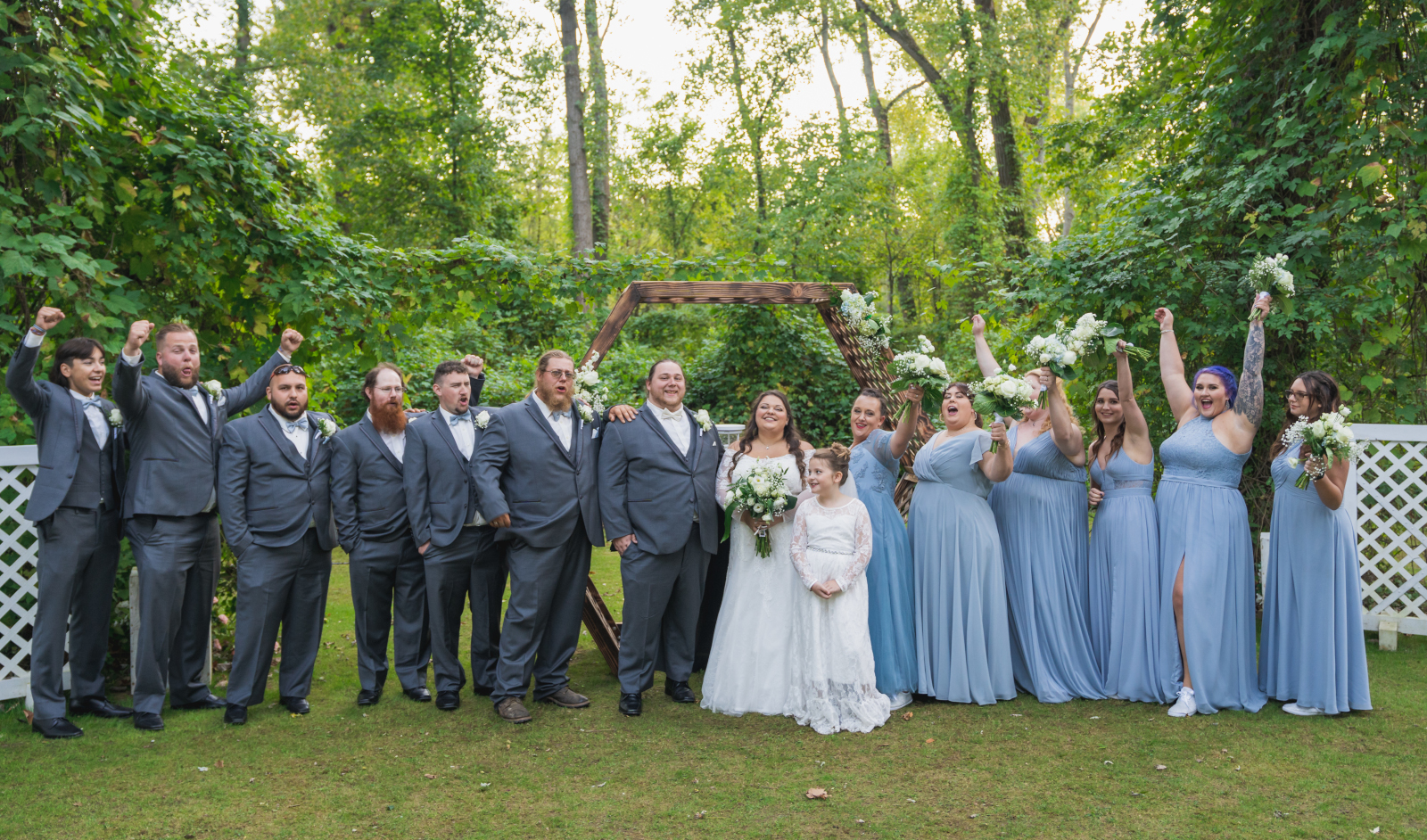 Bride and groom with bridal party, bridal party portrait, fun bridal party portrait, cheering, large bridal party, flower girl, hexagon arch, green, trees, nature, outdoor September wedding ceremony at Westfall Event Center