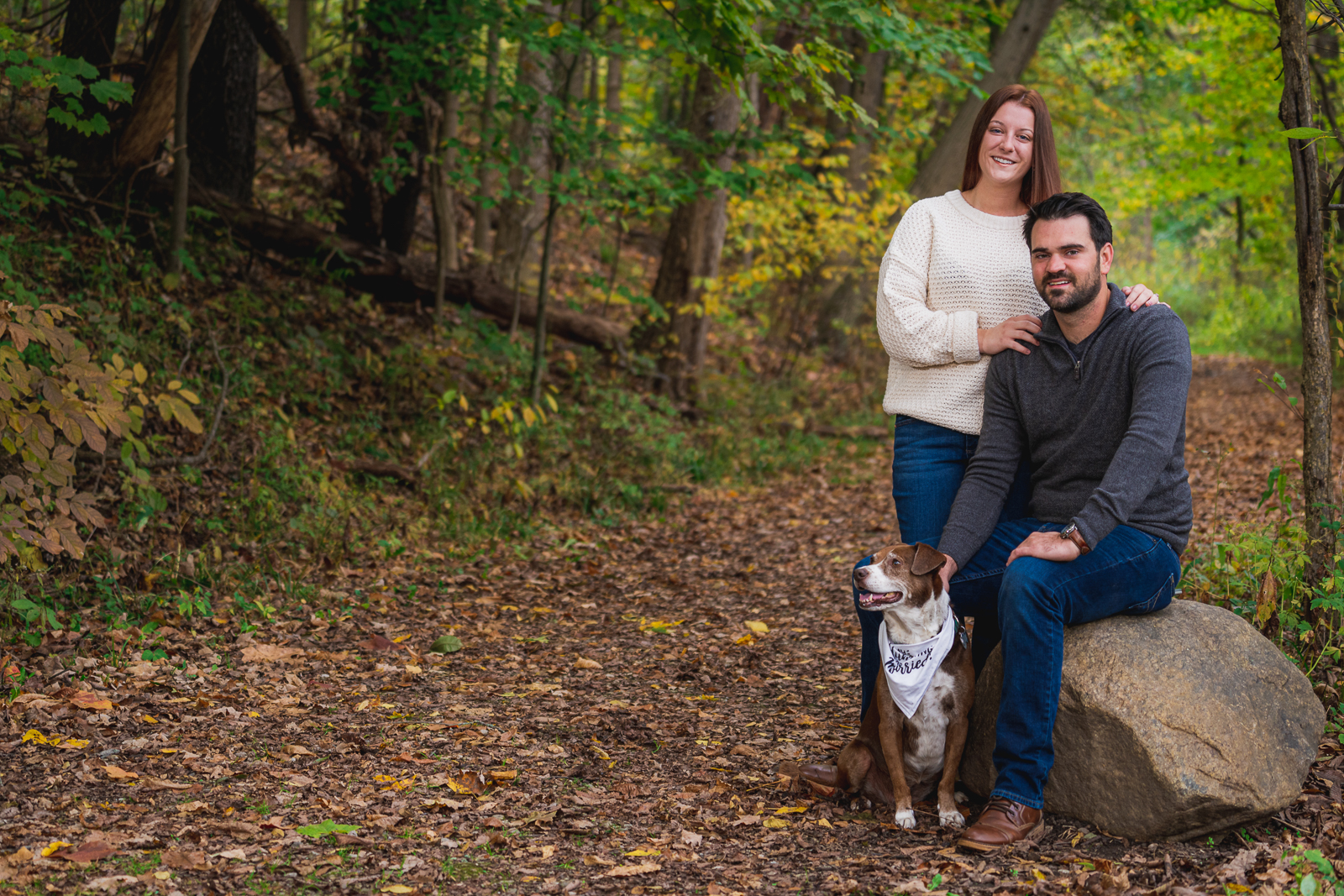 Man and woman fiancee engagement photo with dog, smile, cute dog, dog bandana, outdoor, nature, forest, fall leaves, fall colors, outdoor fall engagement photo session at Tinkers Creek, Bedford Reservation, Cleveland Metroparks
